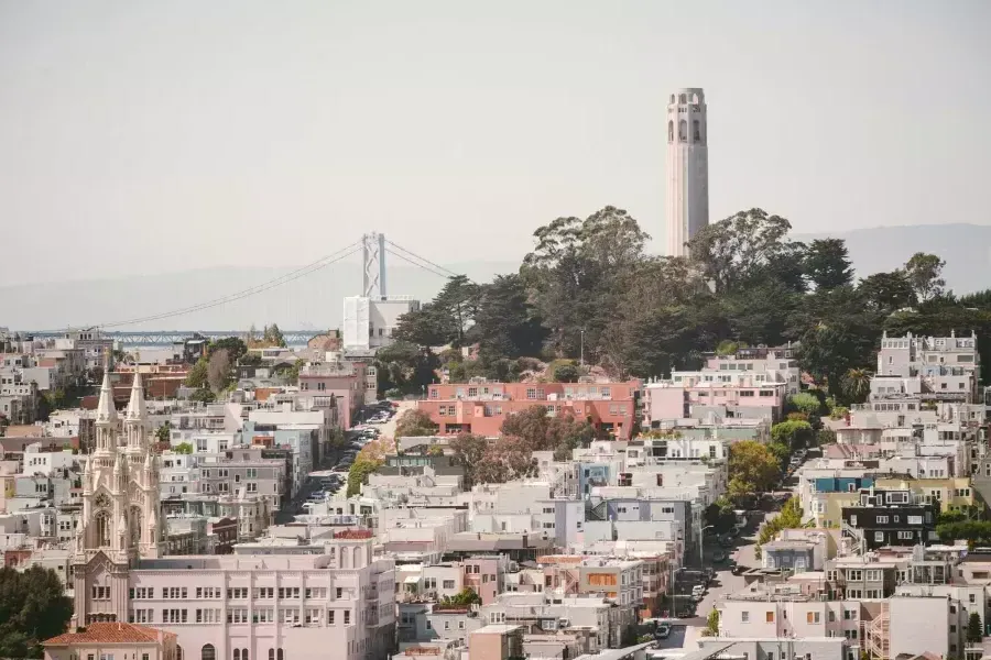 威尼斯人官网平台app的Coit Tower，背景是海湾大桥，全景是一座被房屋覆盖的山丘.